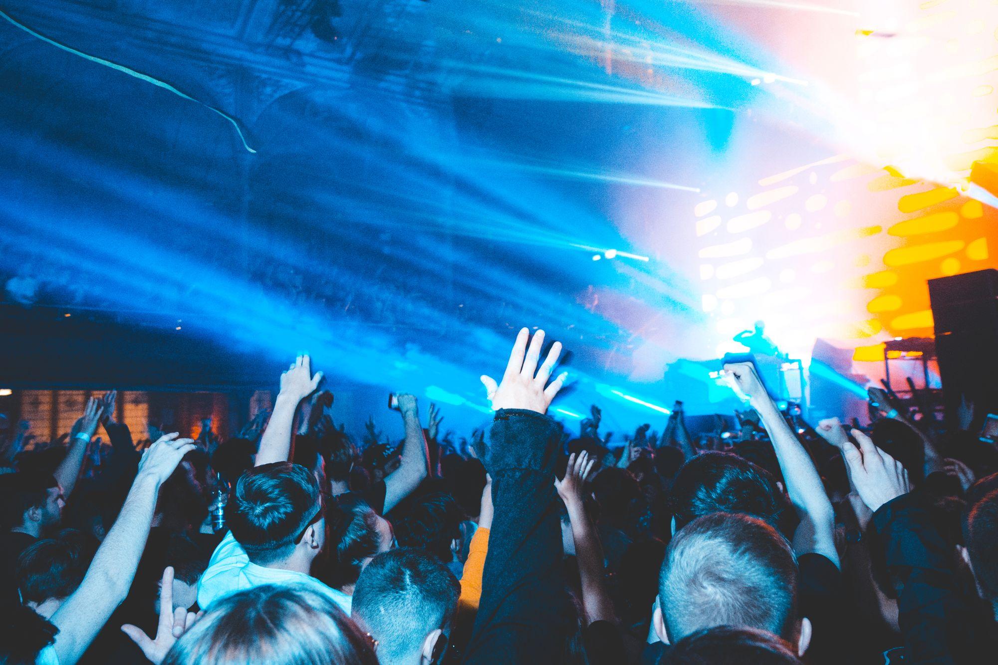 A DJ performing for a crowd with raised hands under blue light.