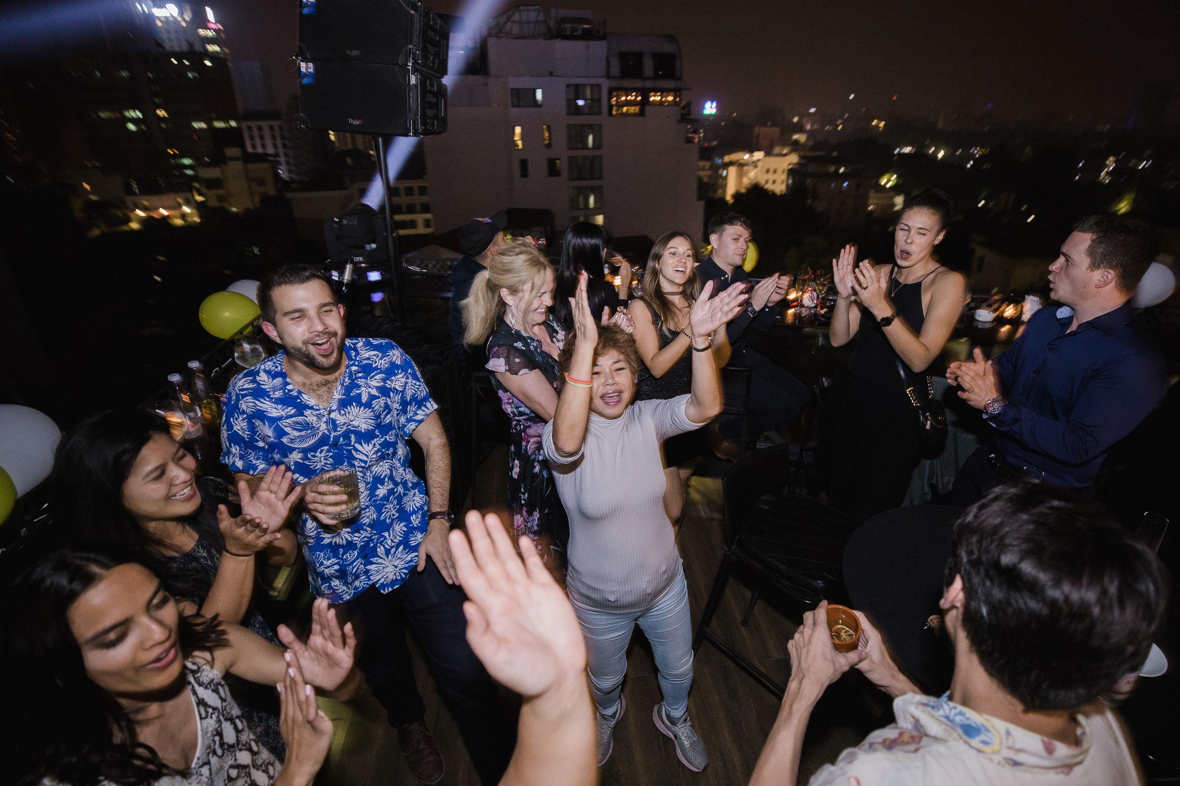Friends dancing at a rooftop party with the city behind them.