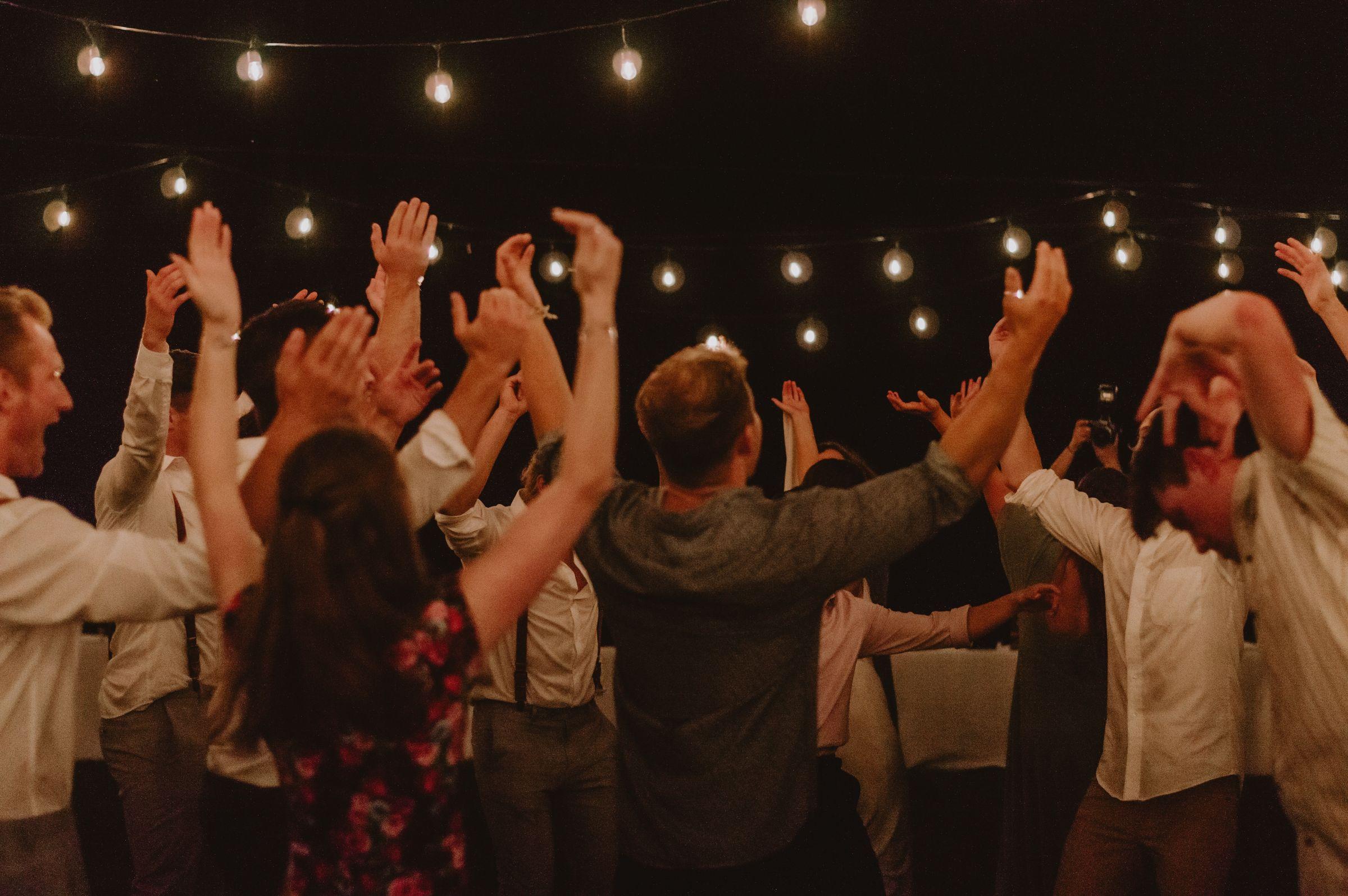 Guests with hands in the air beneath string lights.