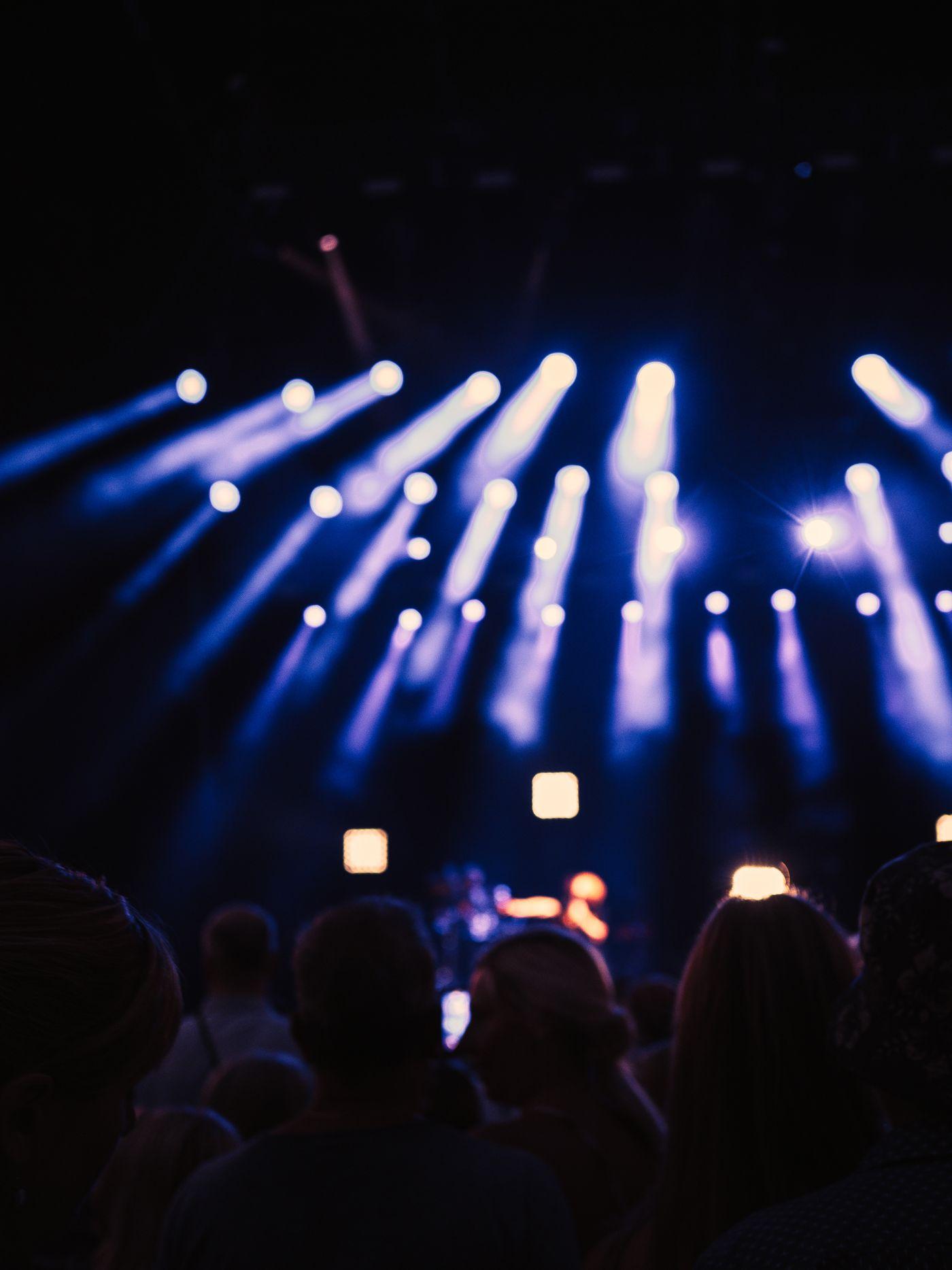 A crowd beneath light beams at an evening event.