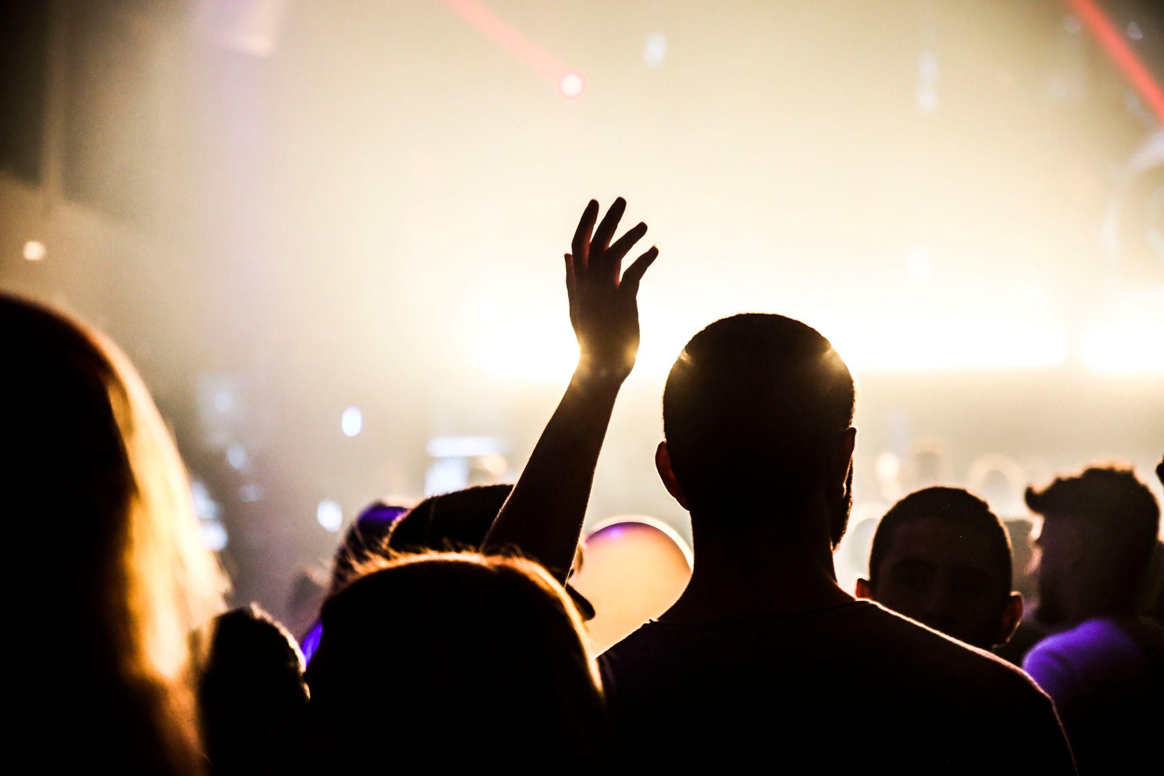 A crowd in silhouette with hands raised under warm backlight on a dance floor.