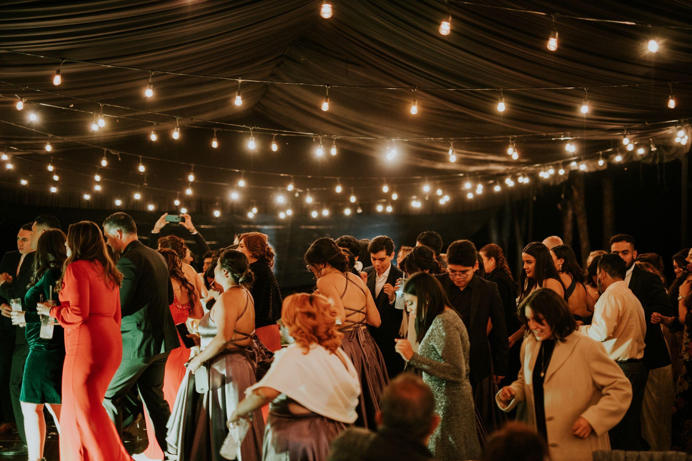 A full tented room of guests under rows of string lights.
